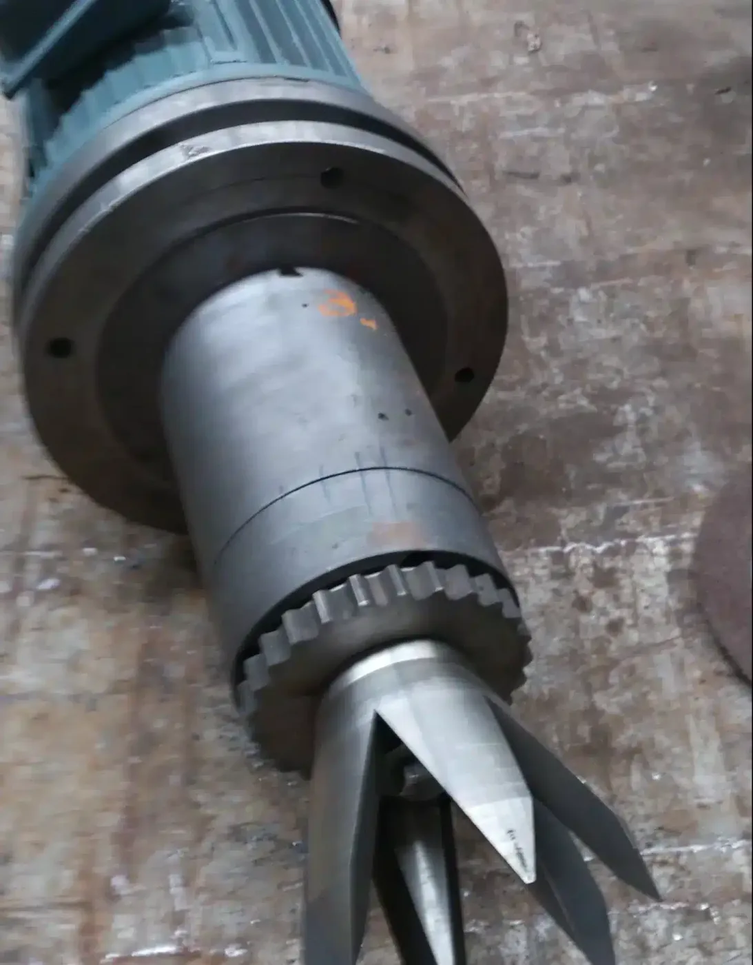 Close-up view of a large industrial ploughshare mixer lying on a concrete surface, with visible wear and corrosion on the metal blades and housing. 犁刀混合机