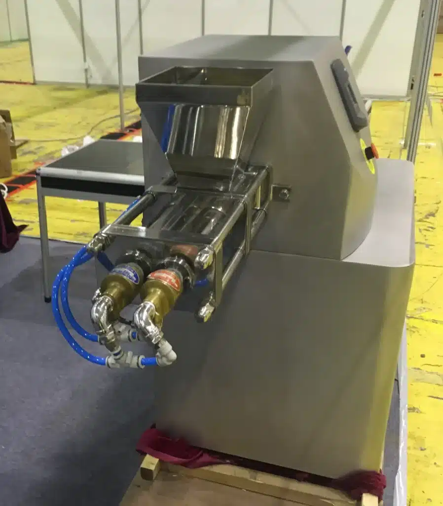 A Screw Extruder for granulation, featuring a hopper, stainless steel body, and intricate screw mechanism, displayed at an industrial expo.